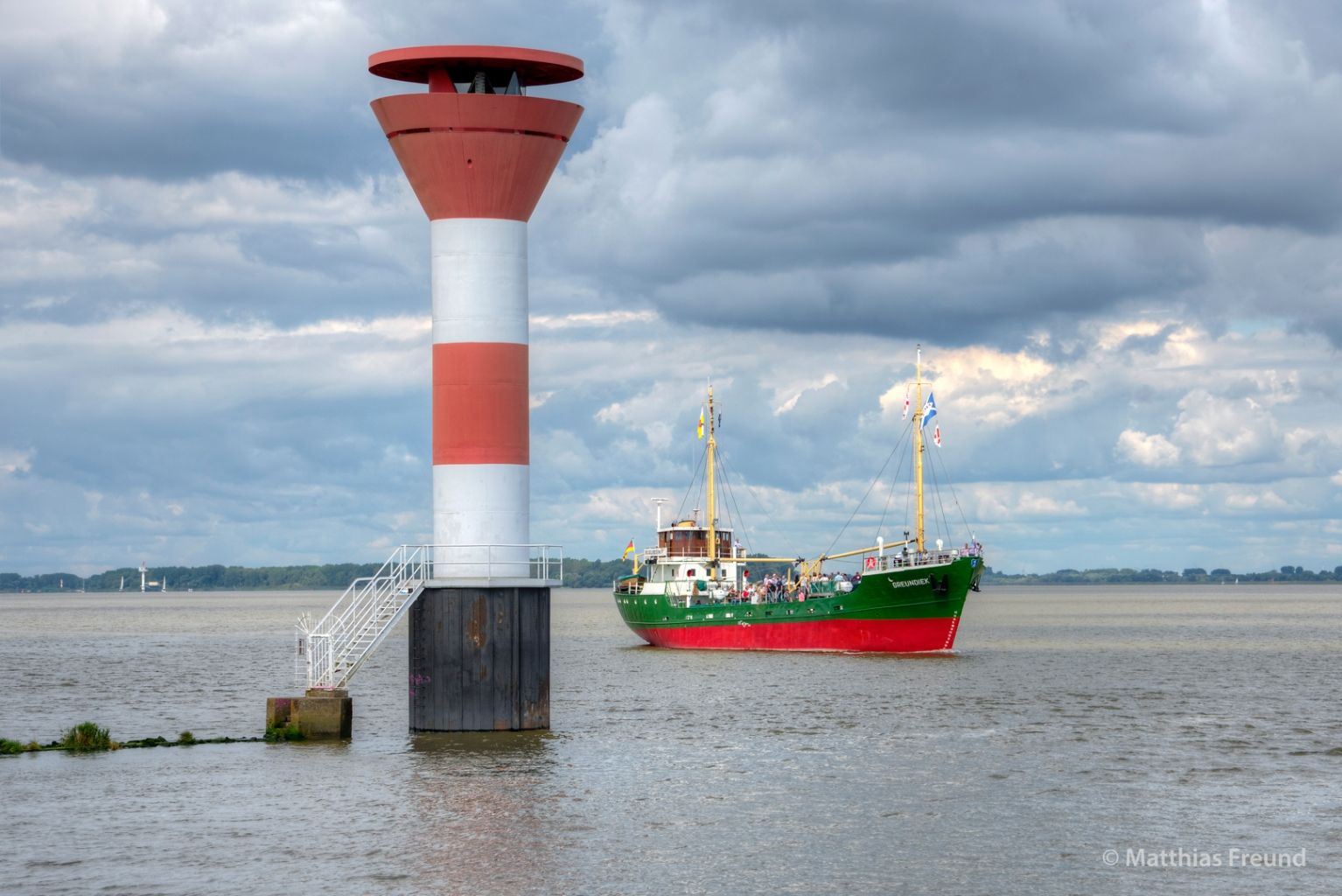 Die Greundiek auf der Elbe, im Vordergrund ein rot-weißer Leuchtturm unter Wolken
