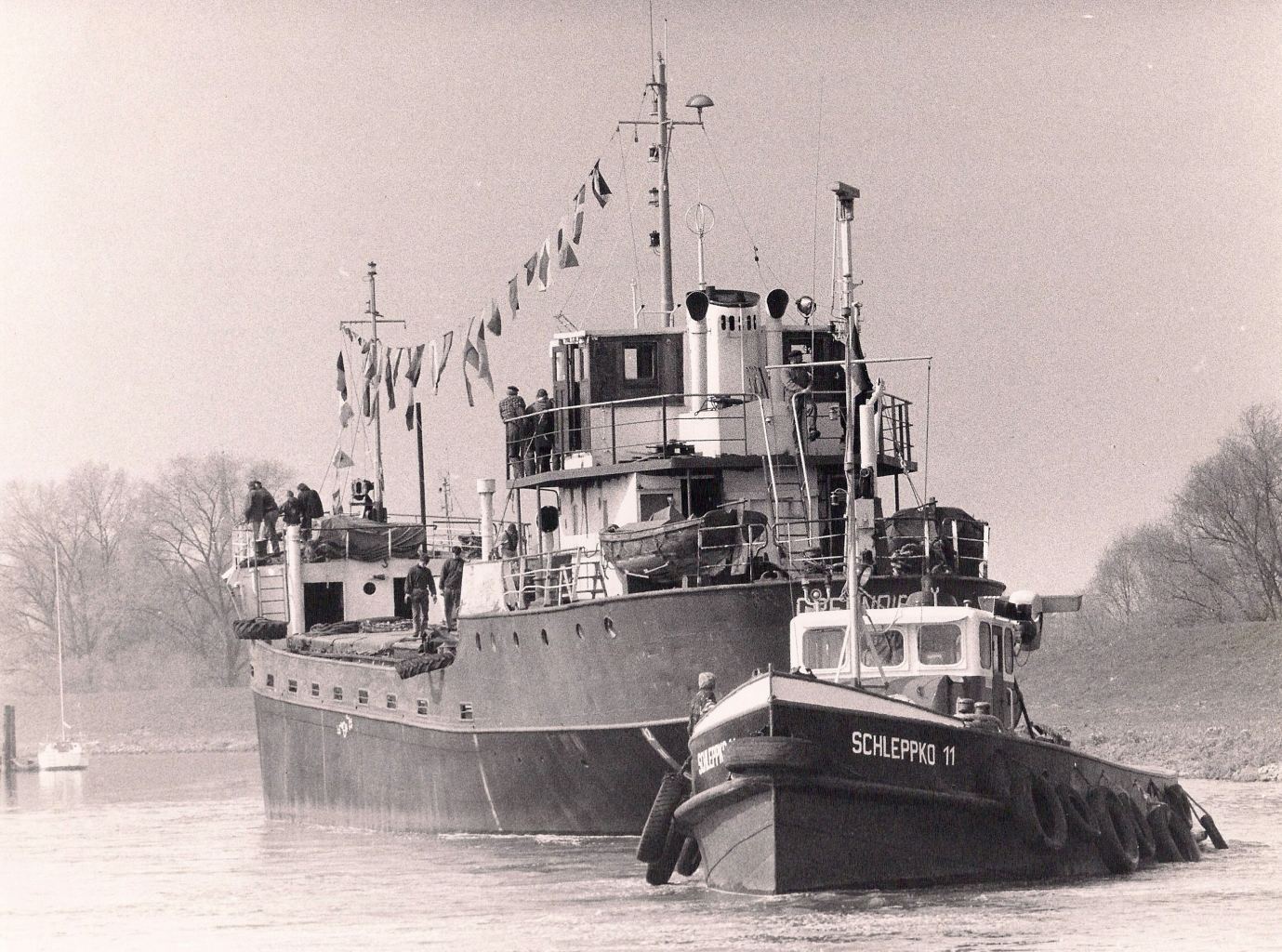 Historische Aufnahme des Schiffs mit Flaggenschmuck und Schlepper